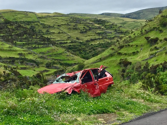 Abandoned and damaged car at the side of a road with hills in the background